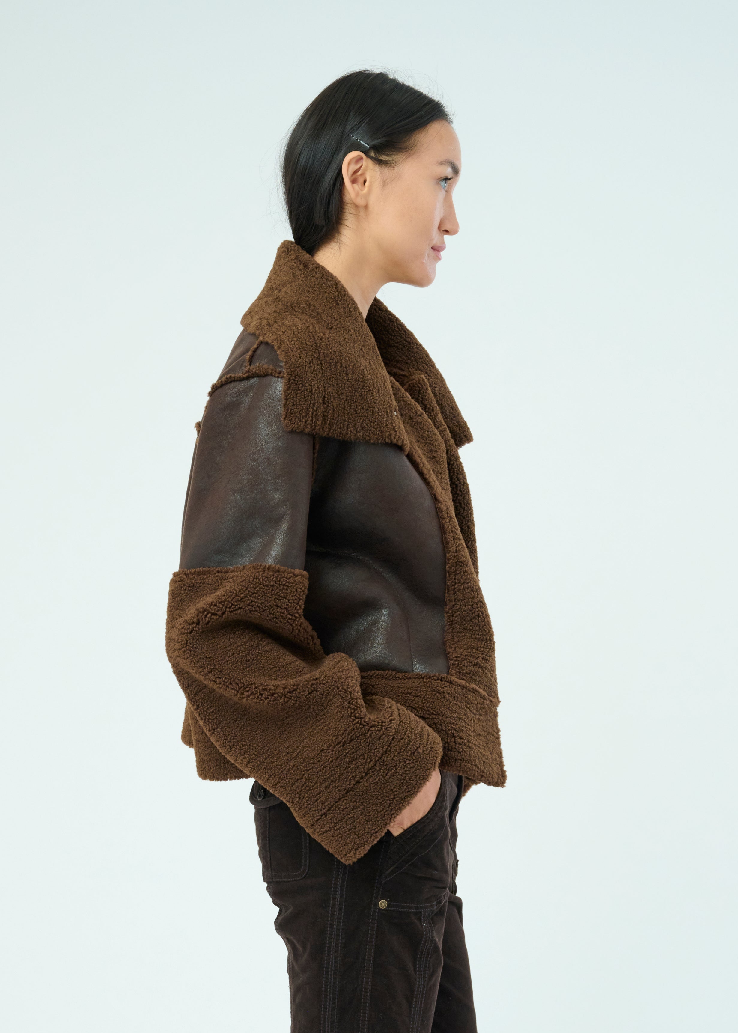 Side view of a tall female model with long black hair confidently posing wearing our dark chocolate colored Trisha Bonded Distressed Suede Sherpa Jacket from Marrakech Clothing.